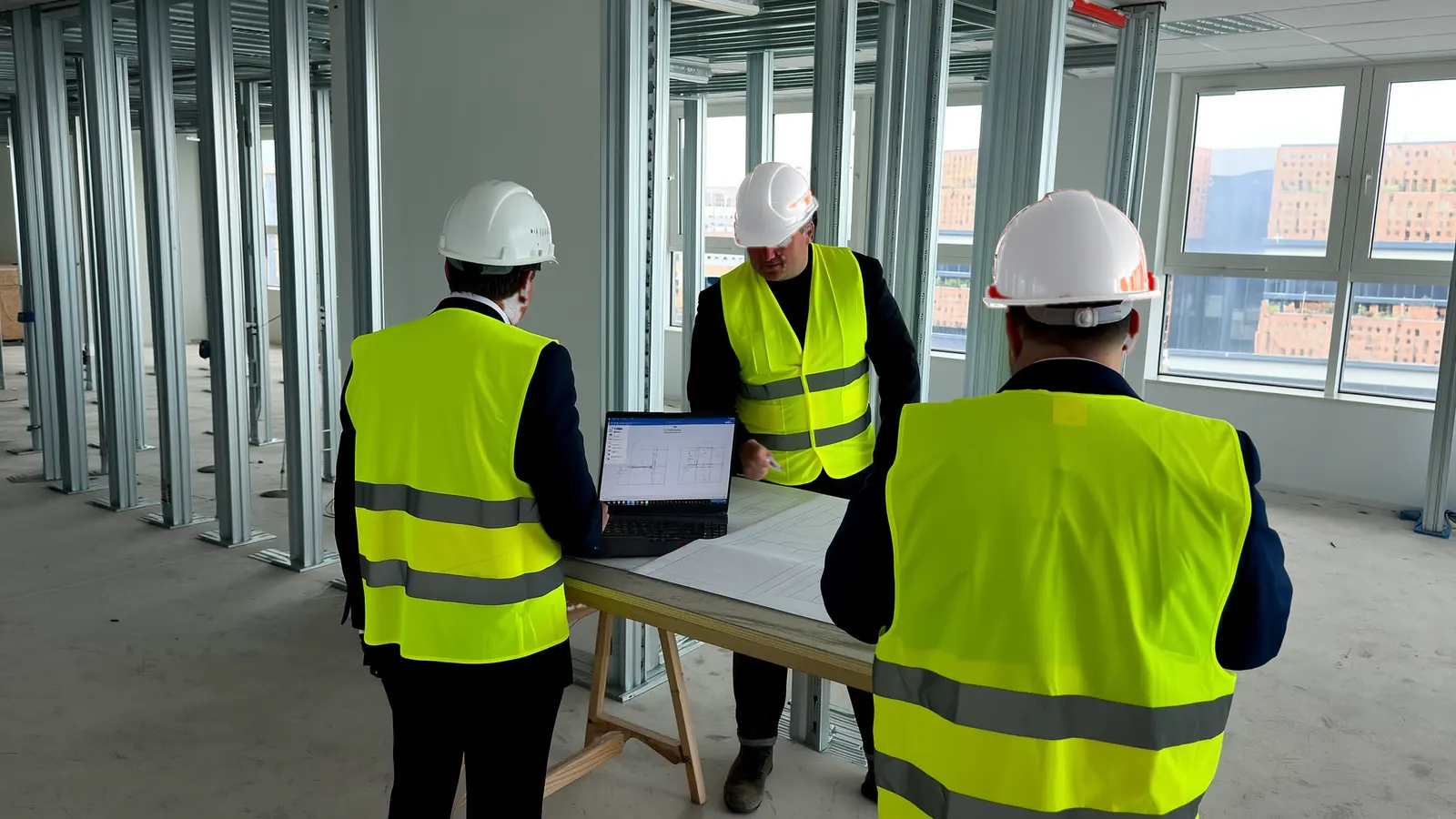 A site meeting around a laptop and drawings on an office floor under fit-out